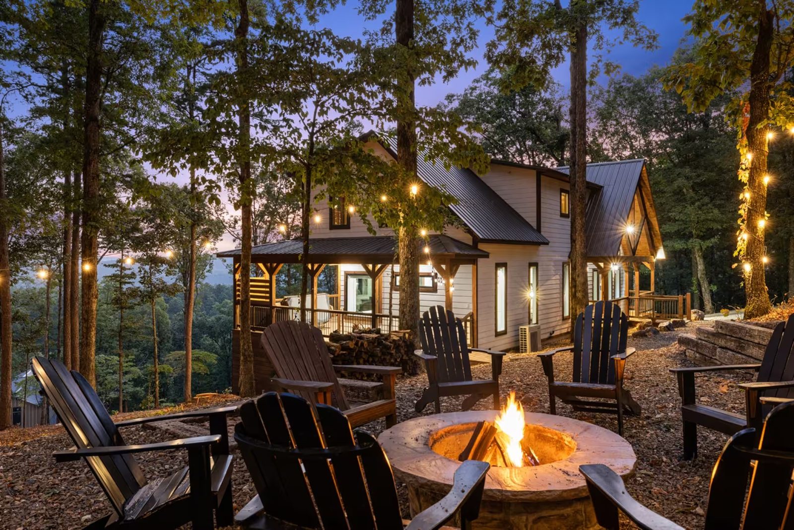 Fire pit with chairs, and the cabin lit behind it at twilight.
