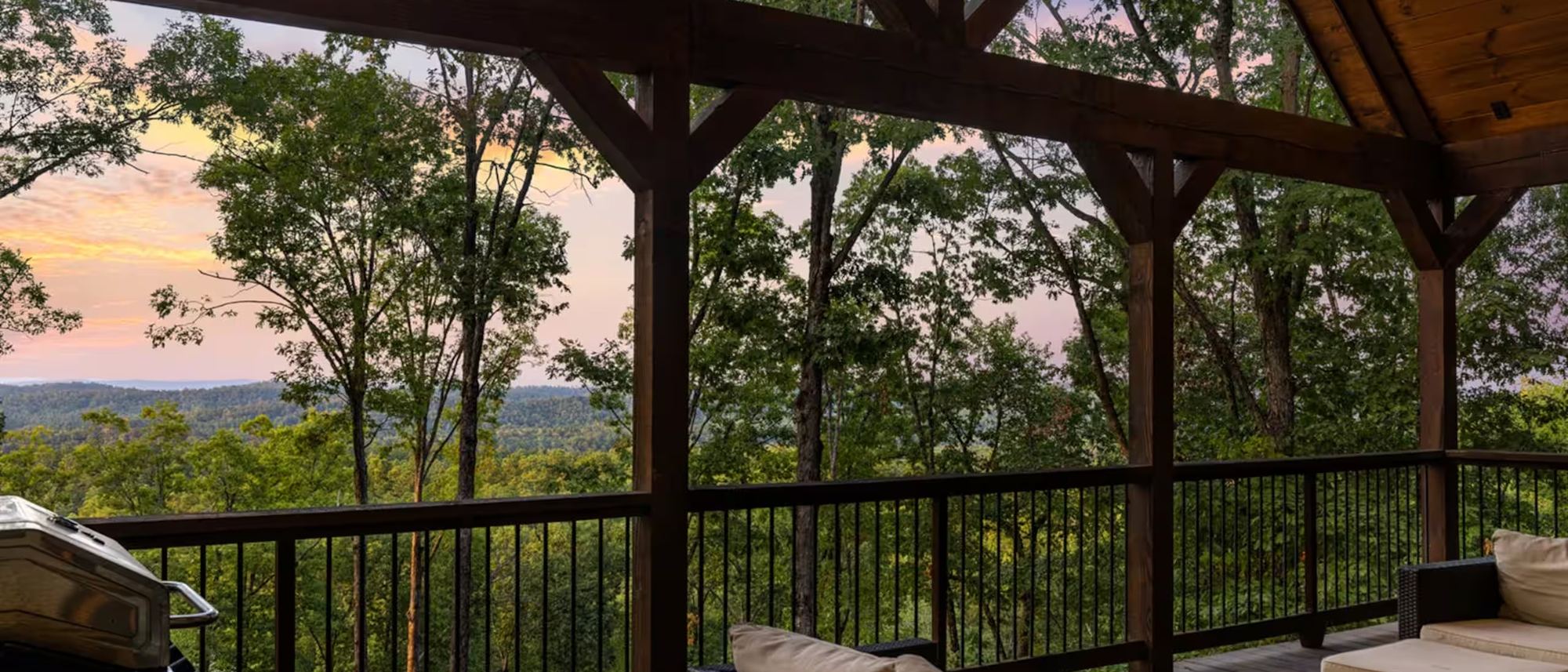 Sunset over a forested ridge, framed by the cabin deck.